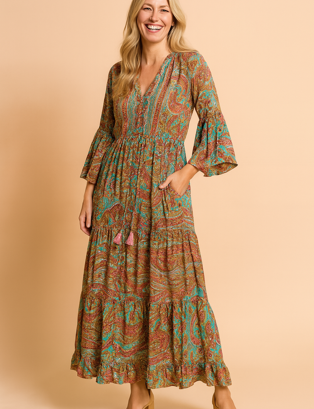 Bohemian-style maxi dress with flared sleeves, gathered waistline, and vibrant paisley pattern in earthy red, turquoise, and green tones, featuring front tassel ties and a tiered hem.