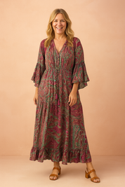 Bohemian paisley maxi dress featuring flared sleeves, a drawstring waist, and tiered hem, designed with vibrant magenta and green swirls in a textured print that remains true to the original pattern.