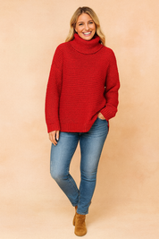 Oversized chunky-knit red turtleneck sweater with ribbed cuffs and hem, paired with medium-wash skinny jeans and tan suede ankle boots.
