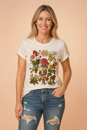 White crew-neck T-shirt featuring a vivid all-over botanical print of assorted wildflowers in rich reds, oranges, pinks, and greens, paired with distressed mid-rise blue jeans.