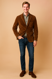 Brown corduroy blazer with notched lapels, three front pockets, and button closure, paired with a plaid button-up shirt, dark denim jeans, and brown suede Chelsea boots.