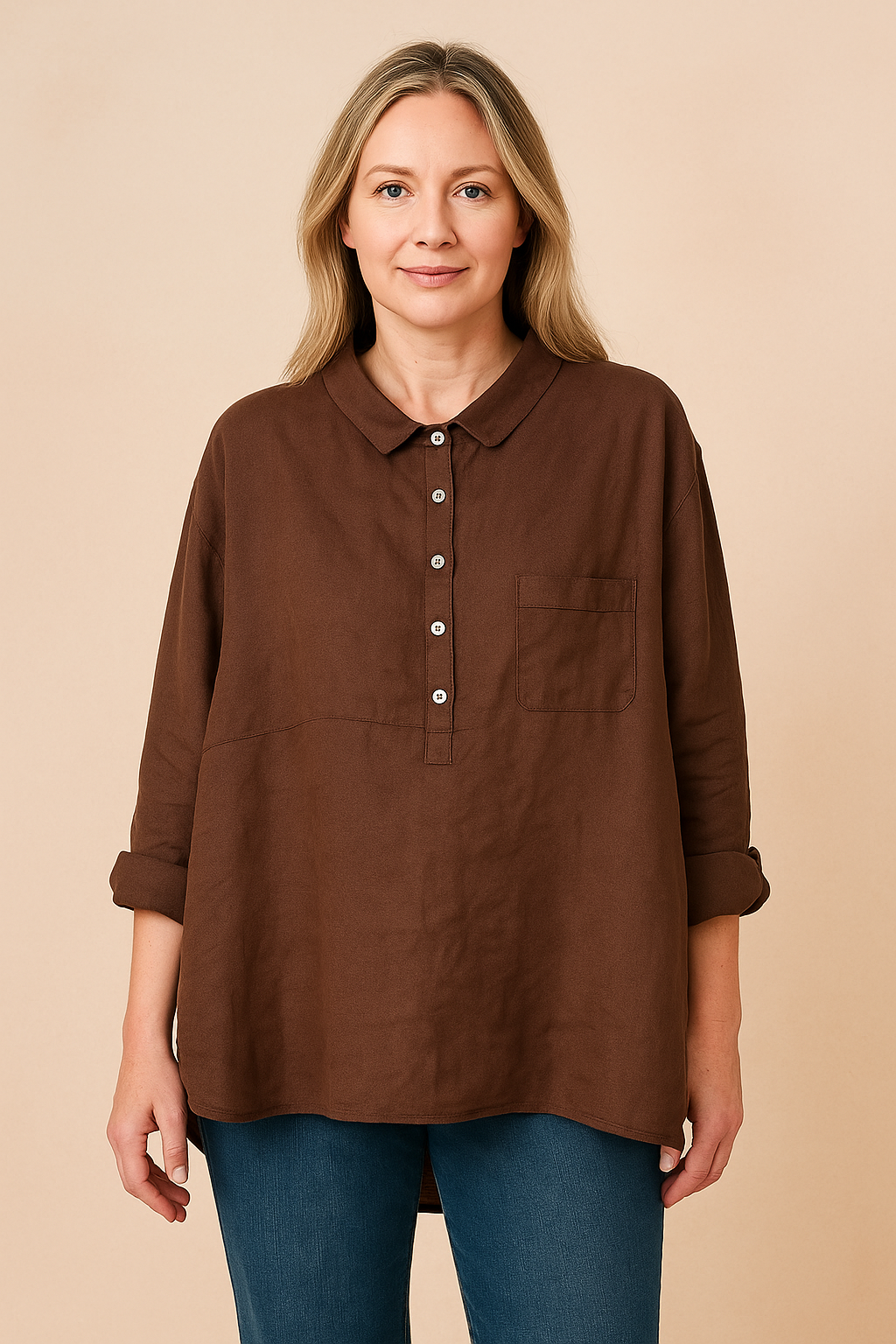 Woman wearing relaxed brown linen shirt with rolled sleeves and collar, paired with blue jeans, on a warm sand pastel background.