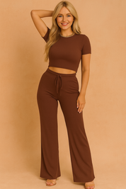 Chocolate brown ribbed two-piece outfit featuring a short-sleeve crop top and high-waisted wide-leg drawstring pants, styled with clear strap heels.