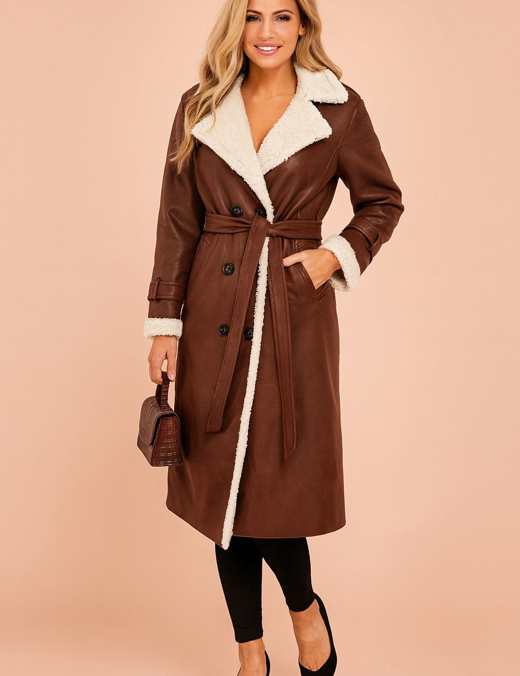 Elegant long brown shearling trench coat with belted waist, double-breasted button design, and contrasting white faux fur lining for a chic winter look.