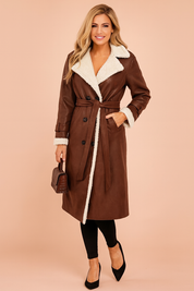 Elegant long brown shearling trench coat with belted waist, double-breasted button design, and contrasting white faux fur lining for a chic winter look.