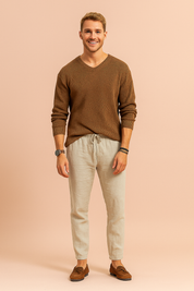 Brown textured V-neck sweater paired with beige linen drawstring pants and brown suede loafers, styled with a leather wristwatch and layered bracelets.