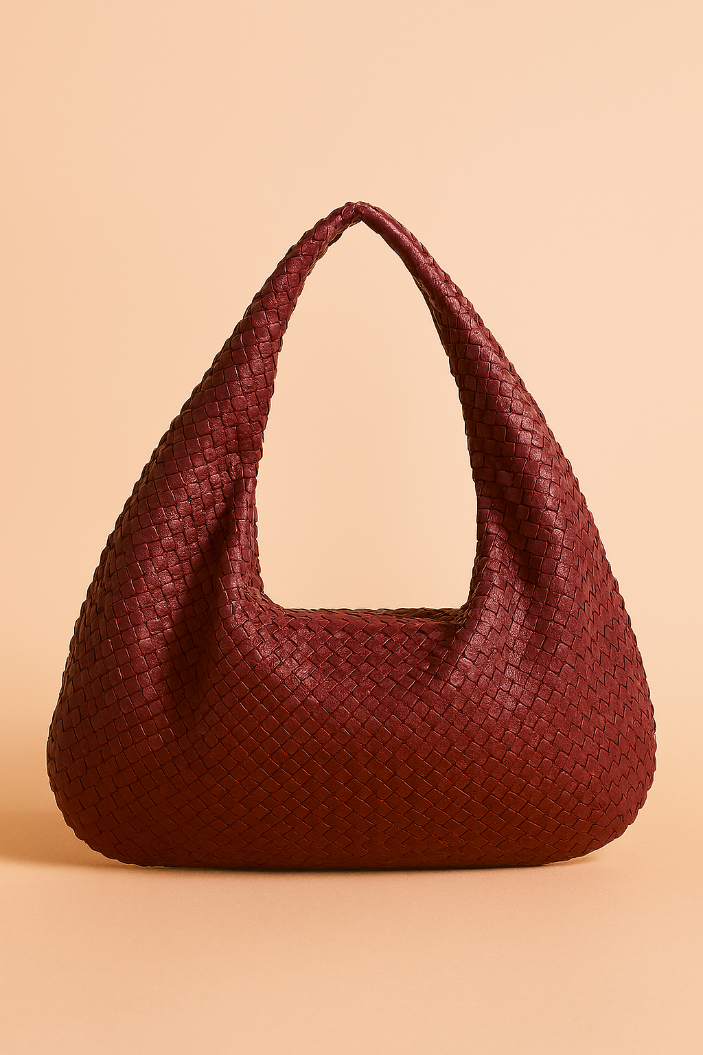 Burgundy woven hobo bag with slouchy silhouette and wide handle, featuring a basketweave texture and soft structure, displayed under studio lighting.