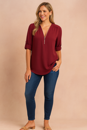 Elegant burgundy zip-up blouse with rolled-up sleeves, styled with dark blue skinny jeans and tan block-heel sandals for a classic, polished look.