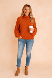 Cozy burnt orange chunky knit sweater with a relaxed fit, ribbed hem, and long sleeves, paired with distressed blue skinny jeans and tan ankle boots.