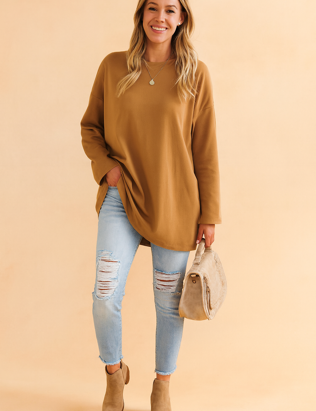 Oversized camel-brown long-sleeve tunic paired with light-wash distressed skinny jeans, taupe suede ankle boots, and a matching beige textured handbag.