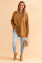 Oversized camel-brown long-sleeve tunic paired with light-wash distressed skinny jeans, taupe suede ankle boots, and a matching beige textured handbag.