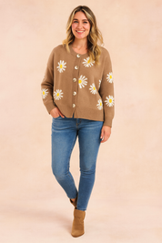 Camel-colored button-up cardigan with white daisy print, paired with medium-wash skinny jeans and tan suede ankle boots.