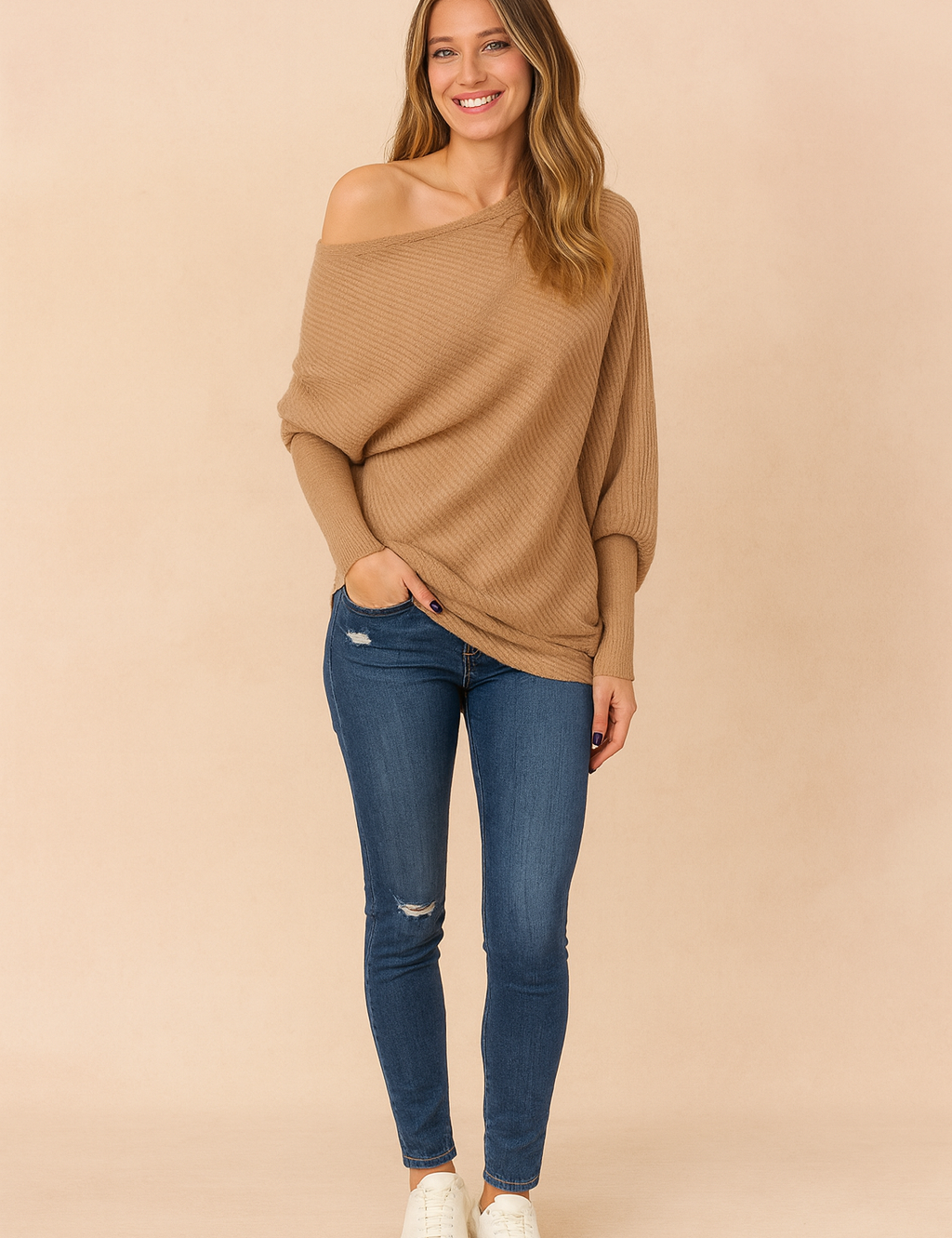 Camel ribbed knit off-the-shoulder sweater paired with distressed blue skinny jeans and classic white lace-up sneakers for a chic casual style.