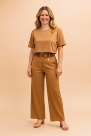 Two-piece camel coord set featuring a structured crop top with short sleeves and matching high-waisted wide-leg trousers. The outfit includes a statement brown belt with gold-tone hardware and a hanging medallion, emphasizing clean tailoring, a smooth matte fabric finish, and seamless vertical creases on the pants for an elongated silhouette.