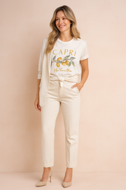 White graphic T-shirt with "Capri" and lemon branch print, paired with cream blazer and tailored trousers, styled in a casual front-knot.