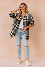 Oversized plaid button-up shacket in black, white, and gray with front flap pockets, styled over a white top, paired with light blue ripped jeans and white sneakers.