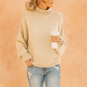 Cream chunky knit turtleneck sweater paired with distressed light blue jeans, styled casually with sleeves slightly rolled and a relaxed fit.