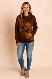 Chocolate brown hoodie with a detailed cat graphic in autumn leaves, paired with distressed blue skinny jeans and taupe suede ankle boots.