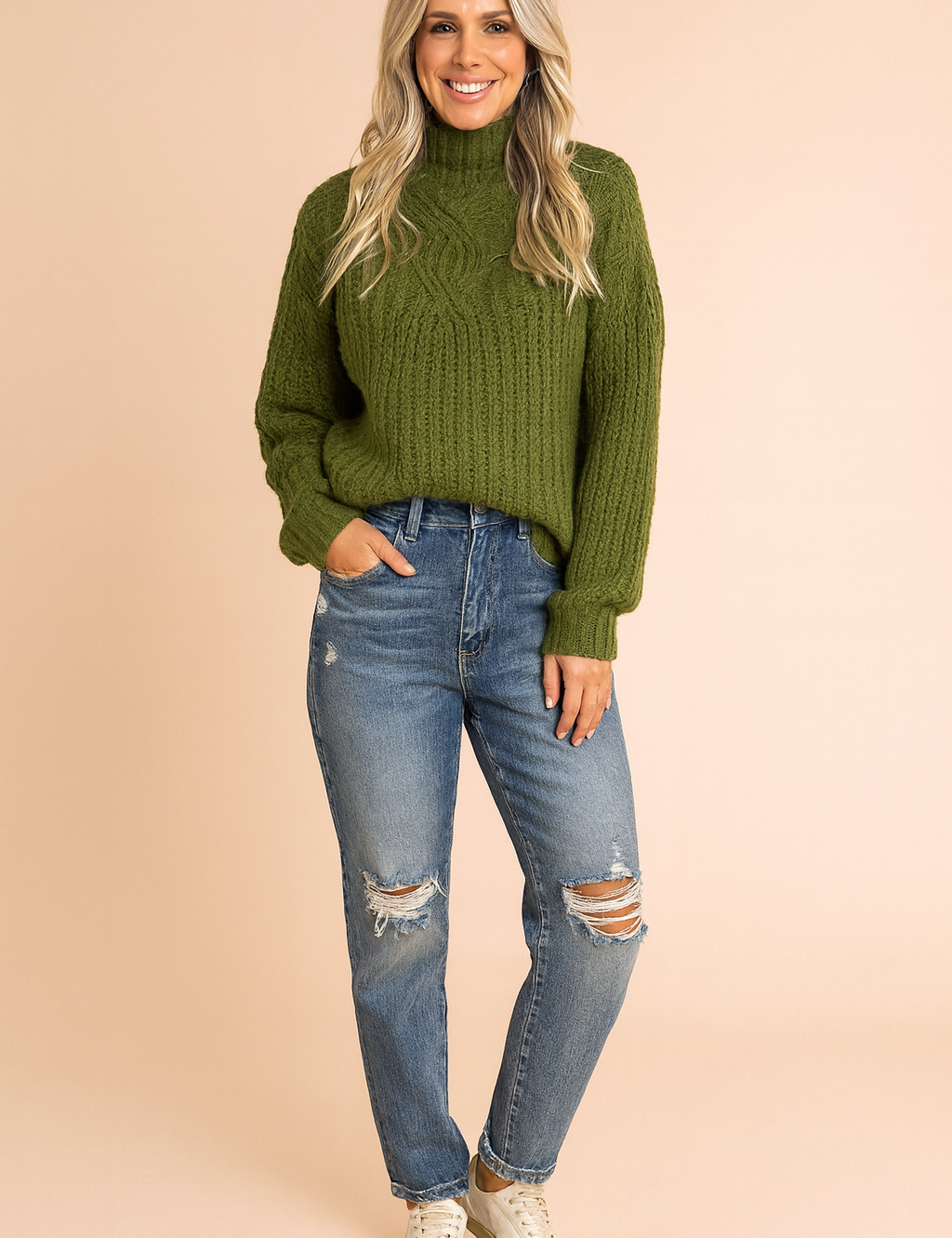 Chunky olive green cable-knit turtleneck sweater paired with distressed blue high-waisted jeans and white low-top sneakers.