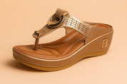 Metallic champagne gold wedge thong sandal featuring perforated detailing on the upper strap, circular gold buckle accent, caramel cushioned insole, and textured tan outsole with a raised "B" monogram on the wedge heel.