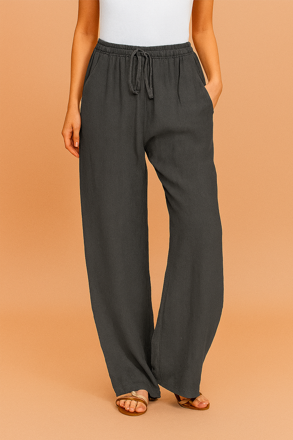 Charcoal gray linen wide-leg pants with a relaxed silhouette, drawstring elastic waistband, and side pockets, styled with flat tan sandals.