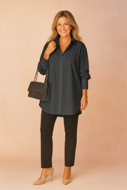 Oversized deep charcoal-gray button-up shirt with crisp collar and long sleeves, styled with slim black pants and a quilted black handbag featuring gold chain detailing.