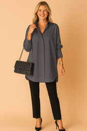 Charcoal gray oversized tunic shirt paired with tailored black pants and a quilted black chain-strap handbag, finished with black pointed-toe heels and minimal gold accessories for a sleek, modern look.