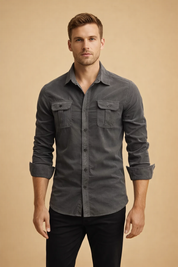 Charcoal grey long-sleeve button-up shirt with pointed collar, tonal front buttons, dual flap chest pockets with button closures, rolled cuffs, tailored slim fit, paired with black straight-leg trousers.