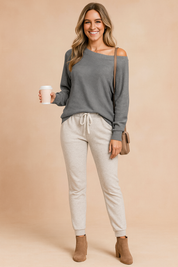  Charcoal gray off-the-shoulder knit sweater paired with light gray drawstring jogger pants and tan suede ankle boots.