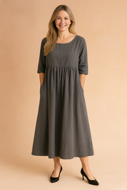 Charcoal gray linen midi dress with elbow-length sleeves, a gathered empire waistline, and side pockets, styled for a casual yet refined look.