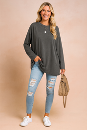 Charcoal oversized long-sleeve top paired with light-wash ripped skinny jeans, accessorized with a layered silver necklace, taupe handbag, and white sneakers.