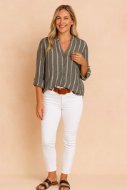 Dark charcoal button-up blouse with vertical white stripes, featuring rolled sleeves and a relaxed fit, paired with fitted white pants and a brown belt.