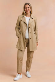 Classic beige trench coat with structured shoulders, notch lapels, and button-front closure, paired with a white crewneck top and tailored beige trousers, styled with white low-top sneakers.