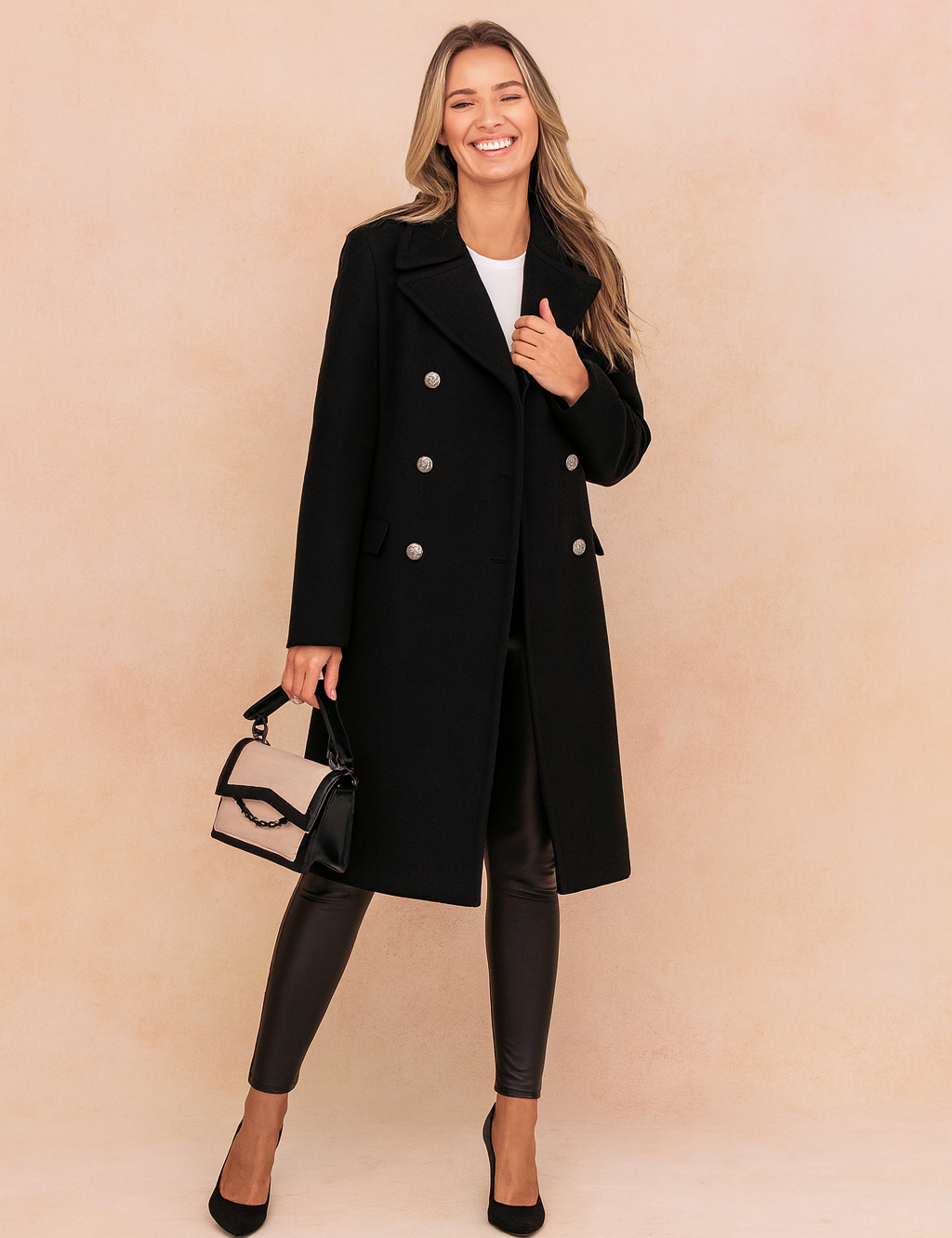 Elegant black double-breasted wool coat with silver-tone buttons, paired with sleek black leather leggings and black pointed-toe heels, complemented by a two-tone beige and black handbag.