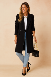 Black long tailored coat with two front buttons styled over a white top and light blue straight-leg jeans, paired with a black leather handbag with a gold chain strap and black pointed heels.