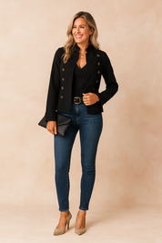 Elegant black military-style jacket with double rows of brass buttons, paired with a black V-neck top, fitted blue skinny jeans, and beige pointed-toe high heels, accessorized with a black clutch and gold necklace.