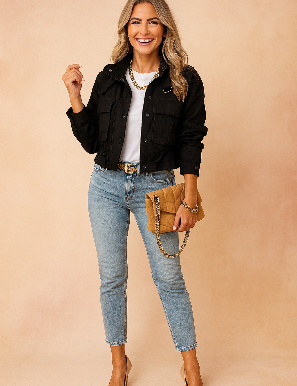 Black cropped utility jacket with front flap pockets and button closure, paired with a white crewneck t-shirt, light-wash high-waisted skinny jeans, camel suede pointed-toe heels, a camel quilted chain-strap clutch, and a gold chain belt.