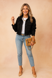 Black cropped utility jacket with front flap pockets and button closure, paired with a white crewneck t-shirt, light-wash high-waisted skinny jeans, camel suede pointed-toe heels, a camel quilted chain-strap clutch, and a gold chain belt.