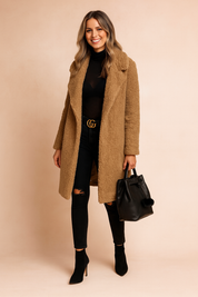  Camel teddy coat with a notched collar, worn over a black turtleneck top and paired with distressed black skinny jeans, a black leather belt with gold buckle, black pointed-toe ankle boots, and a black leather handbag with pom-pom detail.