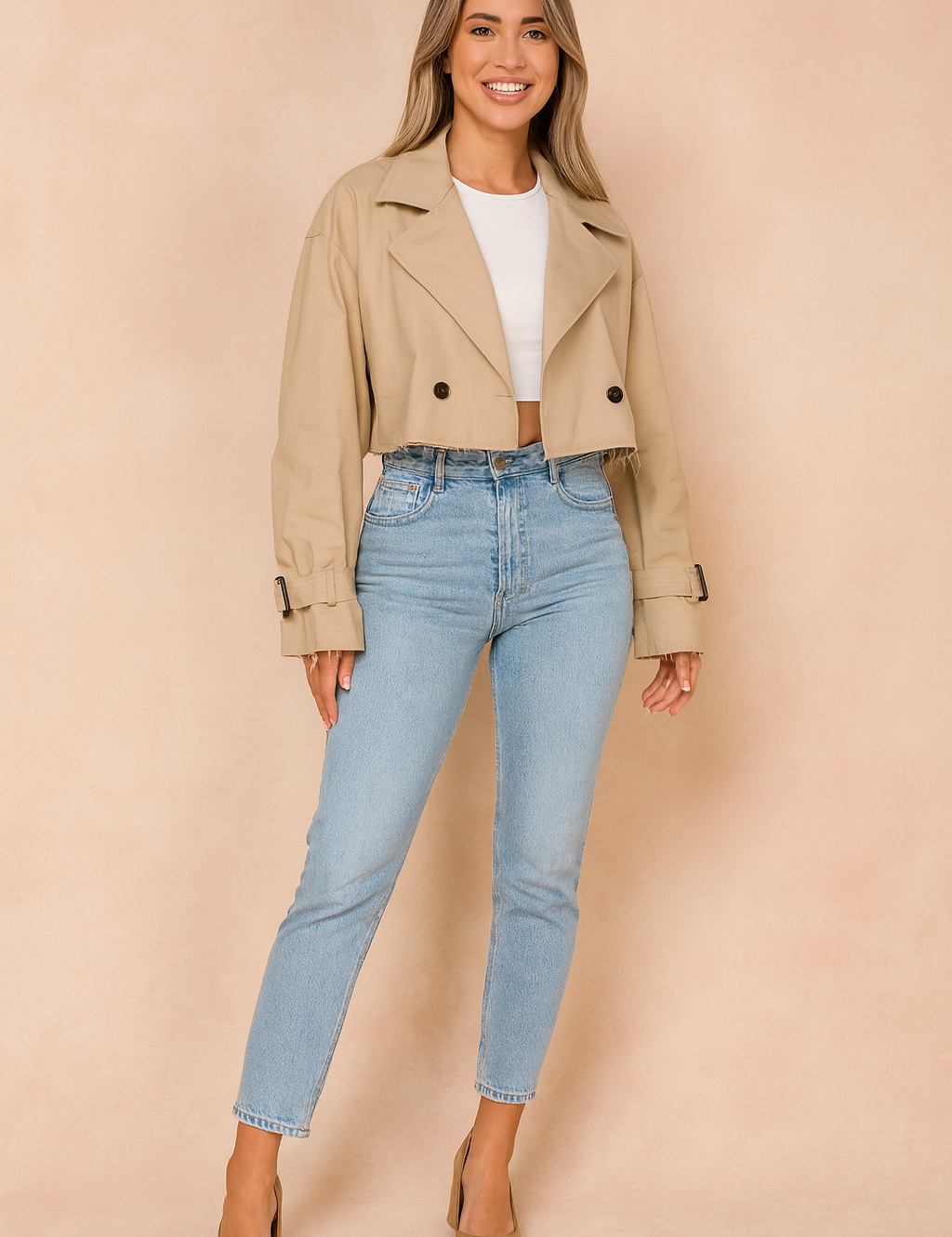 Cropped beige trench coat with black button details, paired with a fitted white crop top, high-waisted light wash jeans, and tan pointed-toe heels.