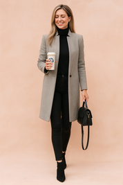 Elegant longline light grey wool coat over a fitted black turtleneck and slim black jeans, paired with black ankle boots and a structured black handbag.