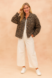 Leopard print button-up jacket with long sleeves, styled over a white top, paired with wide-leg cream trousers and white sneakers.