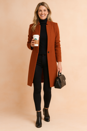 Rust-colored wool coat with a single-button closure, worn over a fitted black turtleneck and black skinny jeans, paired with black ankle boots and a structured black leather handbag.