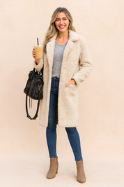 Cream sherpa teddy coat layered over a heather gray knit top, paired with fitted blue denim jeans and taupe suede ankle boots, accessorized with a structured black leather handbag.