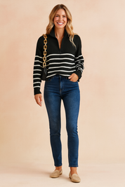 Ribbed black-and-white striped high-collar zip sweater with long sleeves, paired with dark blue slim-fit jeans and beige suede loafers, accessorized with a black leather shoulder bag featuring a chunky gold chain strap.
