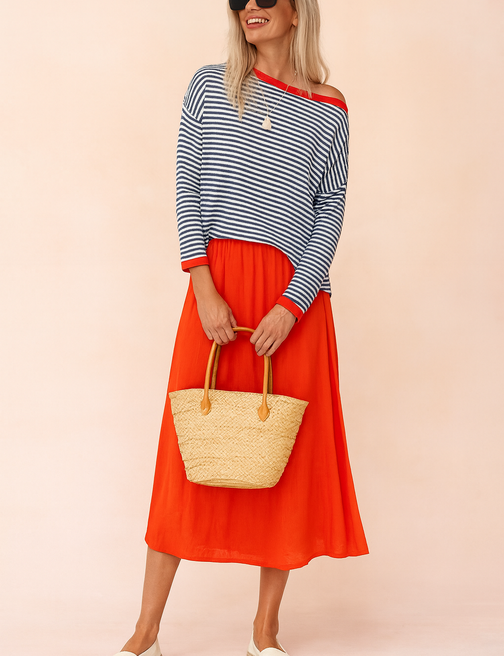 Navy and white striped off-shoulder sweater with red trim, paired with a vibrant red midi skirt, natural woven tote bag, and cream espadrille flats.