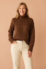 Chocolate brown cable-knit high-neck sweater with braided pattern across the chest and shoulders, paired with cream straight-leg jeans.