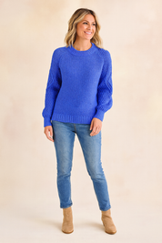 Cobalt blue knit sweater with textured sleeves and ribbed cuffs, paired with light blue jeans and tan suede ankle boots.