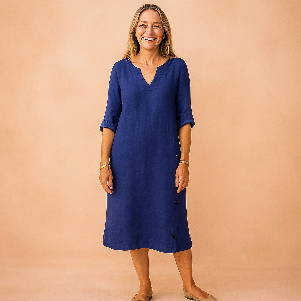 Relaxed-fit cobalt blue linen dress with a modest V neckline, 3/4 rolled sleeves, and side button detailing, styled with simple gold bracelets and neutral slip-on flats.
