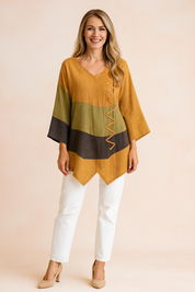 Loose-fit V-neck tunic with mustard, olive green, and charcoal color blocking, featuring asymmetrical hemline and decorative zigzag stitching on the front.